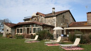 A stone house with a balcony, a covered patio with lounge chairs, and a large window overlooking the garden. - Domaine Castetbieilh (Tercis-les-Bains)
