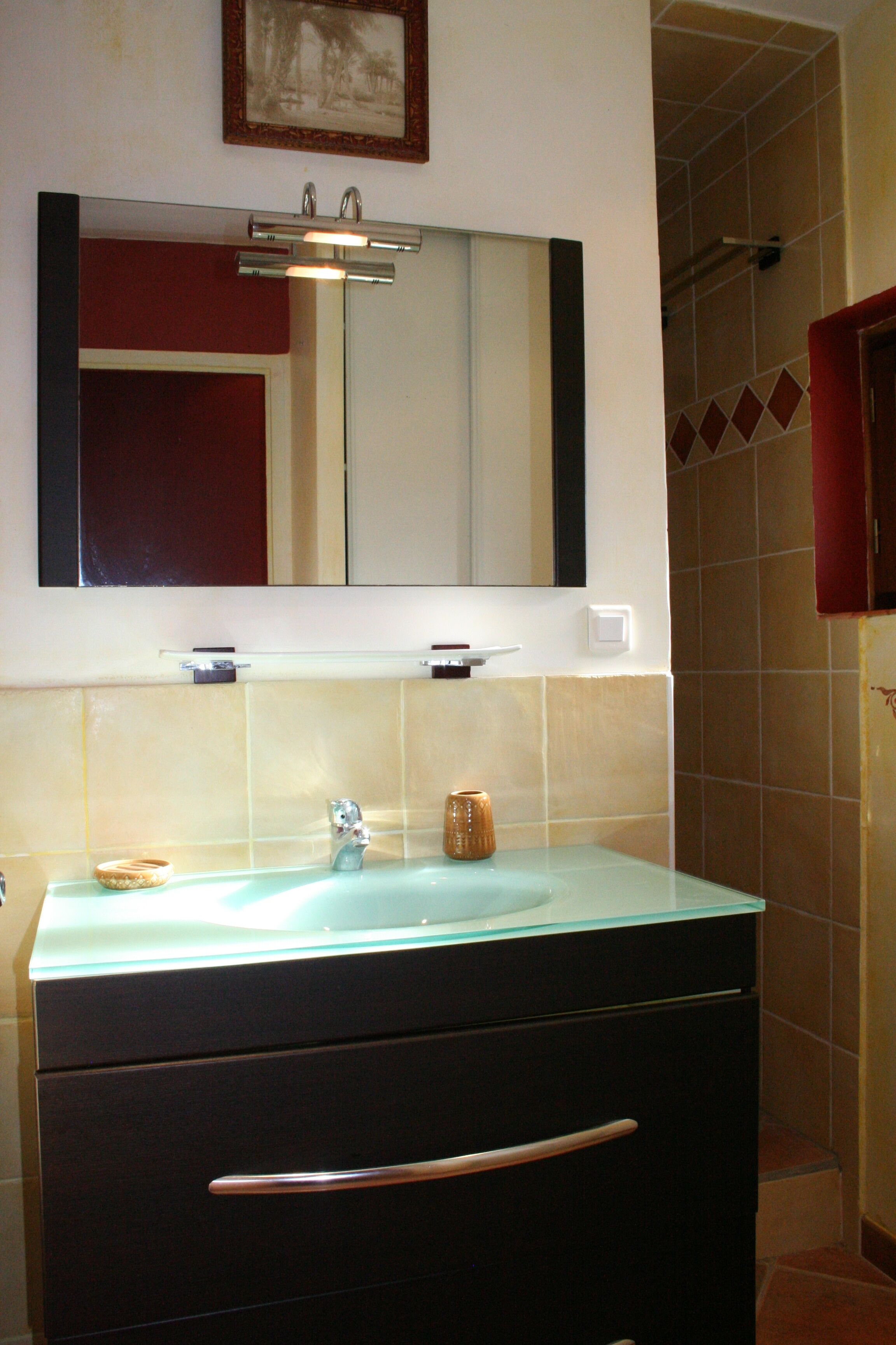 Un baño con un lavabo de vidrio, un espejo encima y un mueble oscuro debajo.