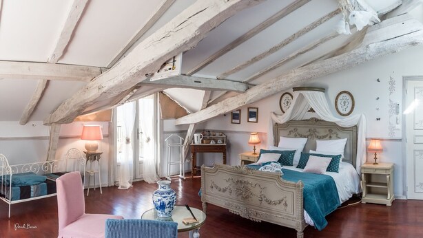A bedroom with a large bed, a chair, a small table, and a lamp. There is a window with curtains and a door with a mirror. - Domaine Castetbieilh (Tercis-les-Bains)