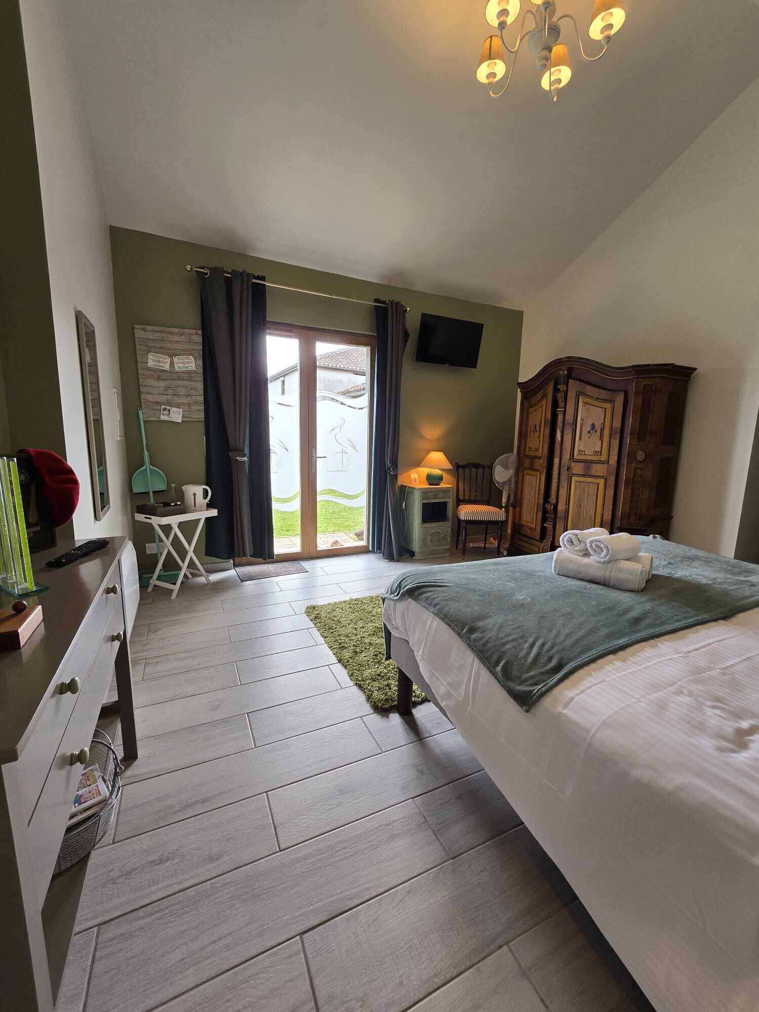 A bedroom with a bed, a desk, a chair, a TV, and a view through a sliding door.