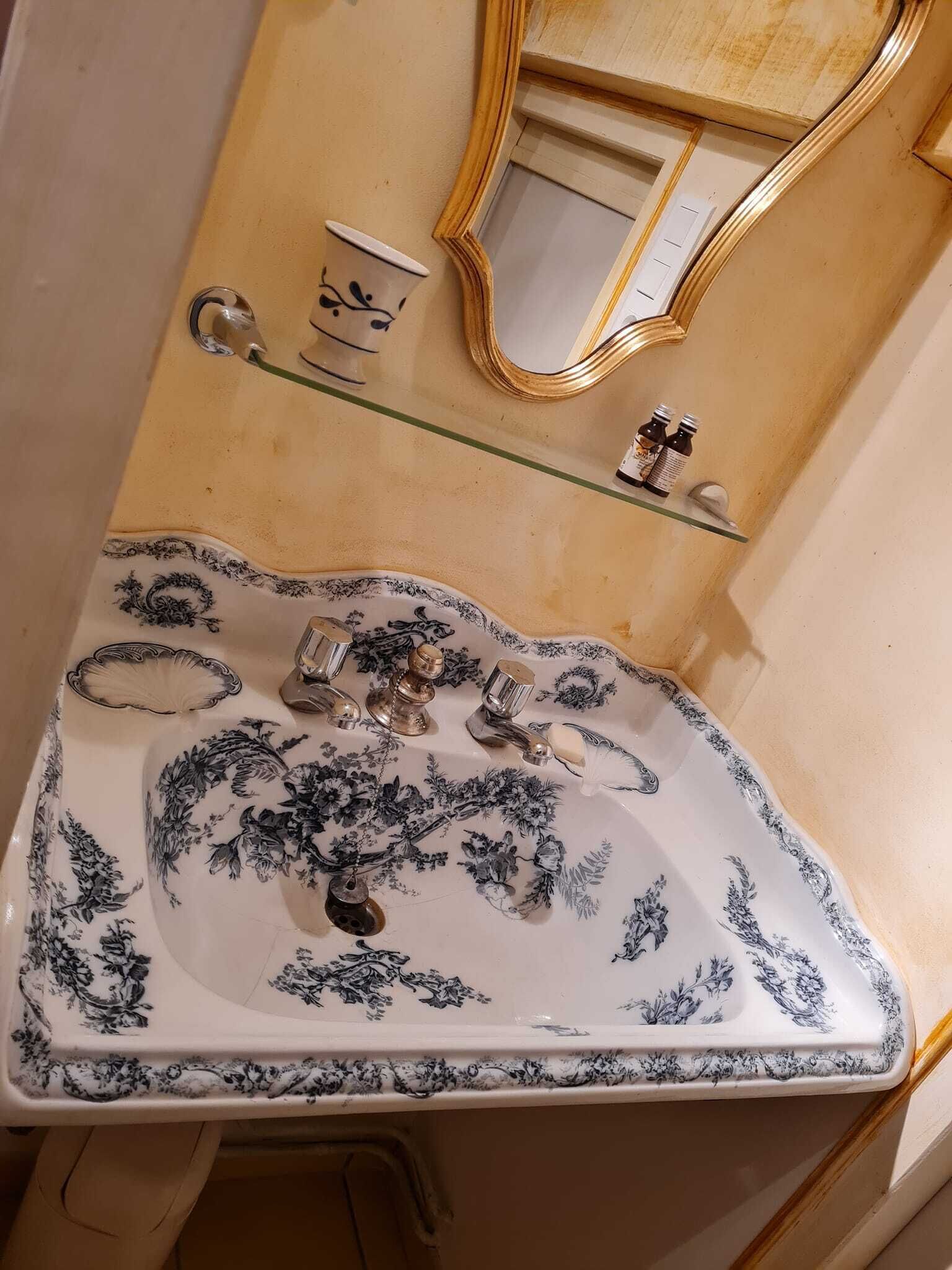 Un baño con lavamanos estampado con motivos florales, un espejo y un pequeño estante con artículos de aseo.