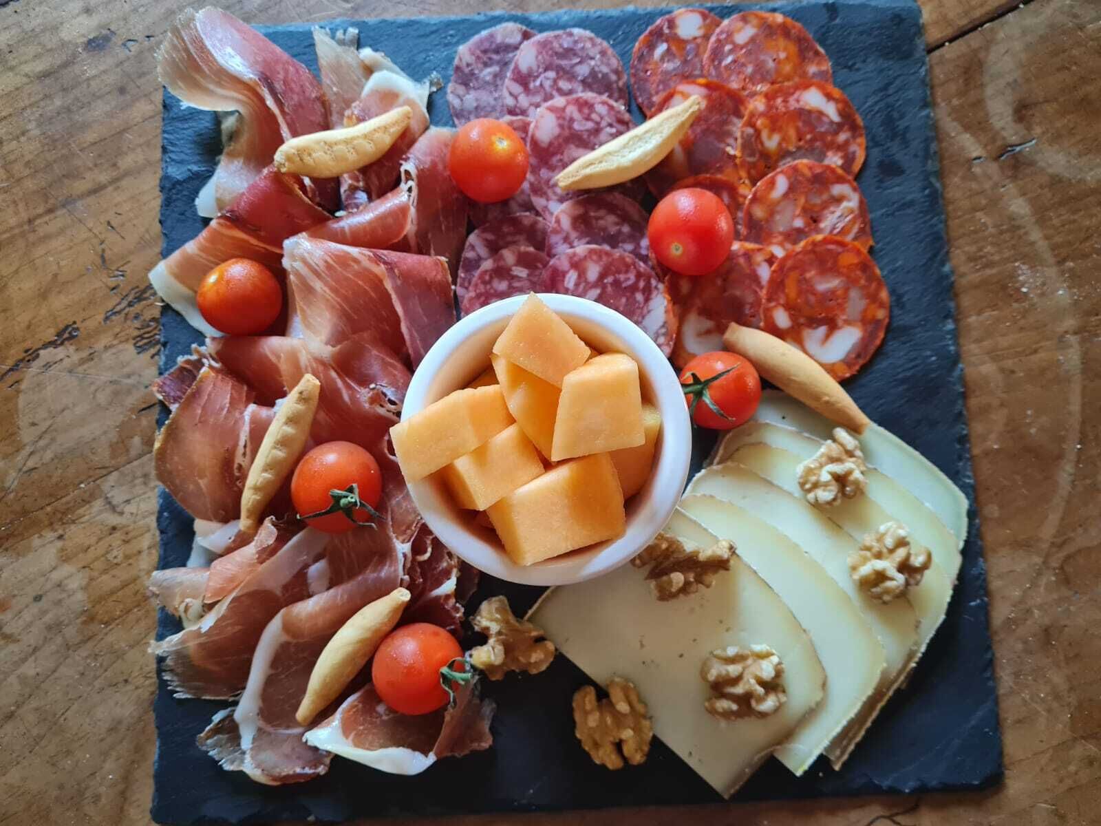 Una tabla de fiambres con diferentes carnes, quesos y frutas.