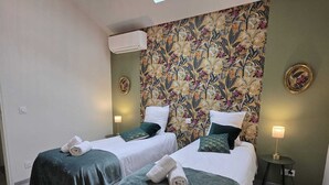 A bedroom with two beds, a skylight, floral wallpaper, and a small table with a lamp. - Domaine Castetbieilh (Tercis-les-Bains)