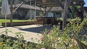 A rustic outdoor seating area with a wooden pergola, a bar sign, and a stone building in the background. - Domaine Castetbieilh (Tercis-les-Bains)