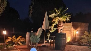 A nighttime outdoor pool area with a wooden deck, a potted plant, and a table with chairs. - Domaine Castetbieilh (Tercis-les-Bains)