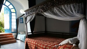 A four-poster bed with a canopy, a small bedside table, and a view of a blue door and steps leading outside. - Dimora Coloniale B&B (Forio)