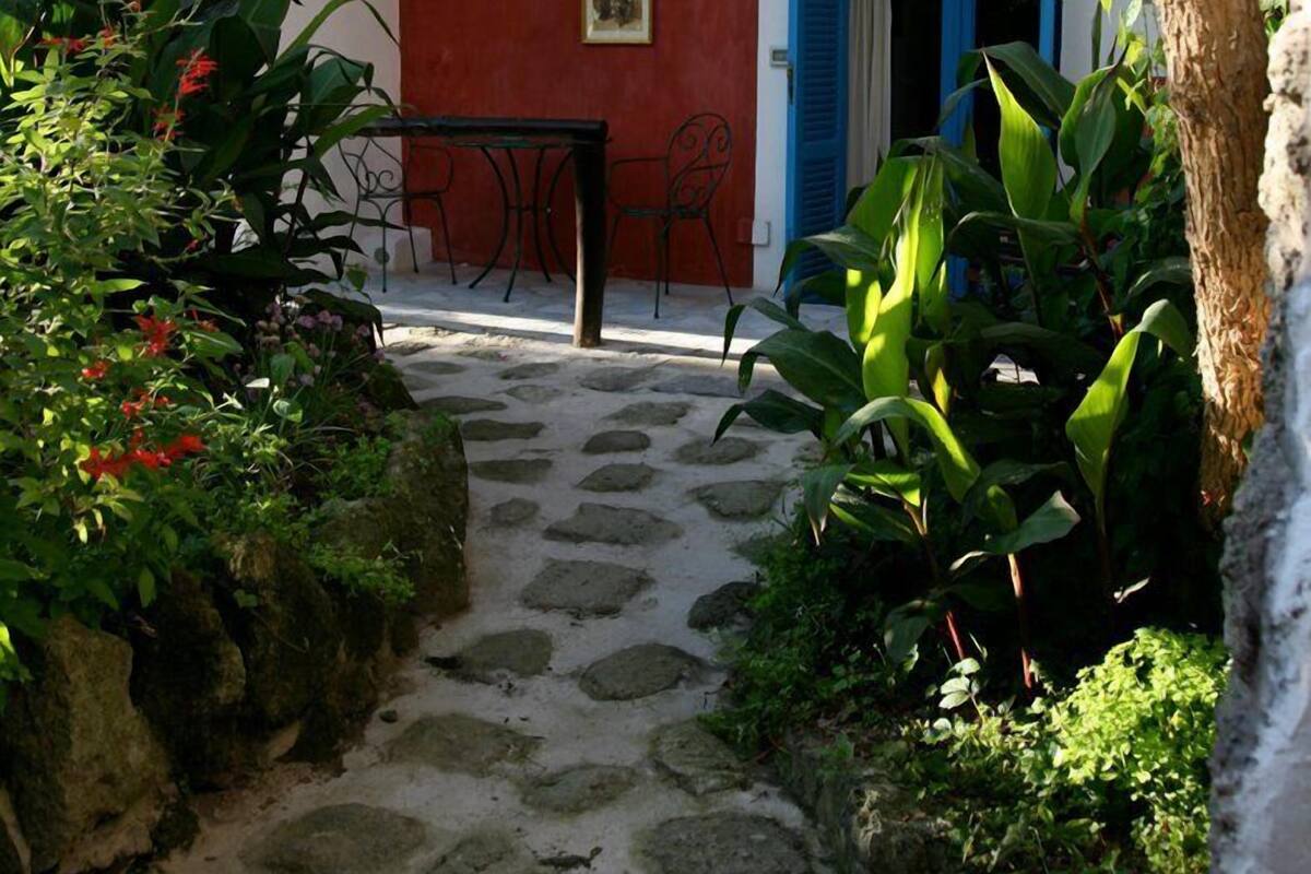 Un sendero de piedra que conduce a un edificio de paredes rojas y azules, con una mesa y sillas afuera.