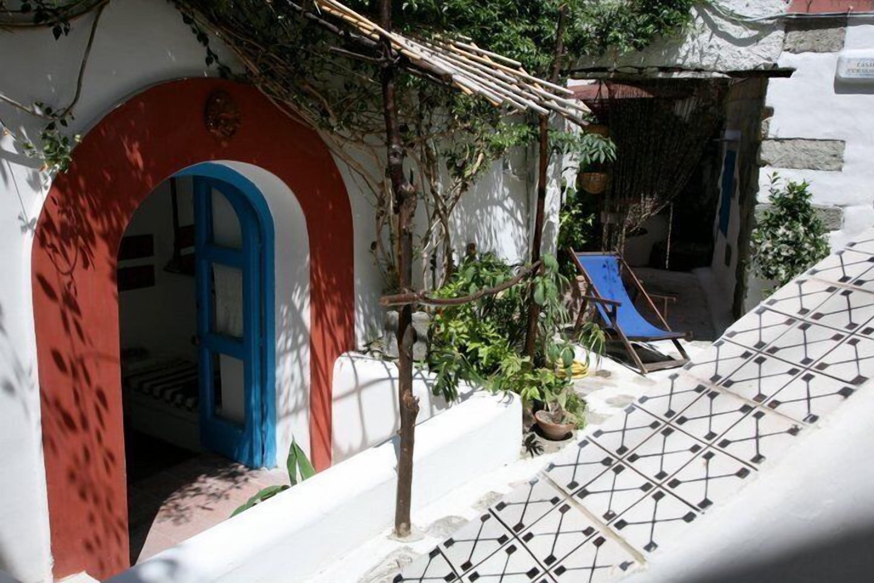 A white building with a red archway and a blue door, a small tree, and a tiled floor.