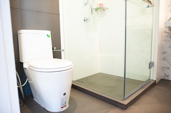 A modern bathroom with a toilet, a glass shower enclosure, and a marble-tiled wall.