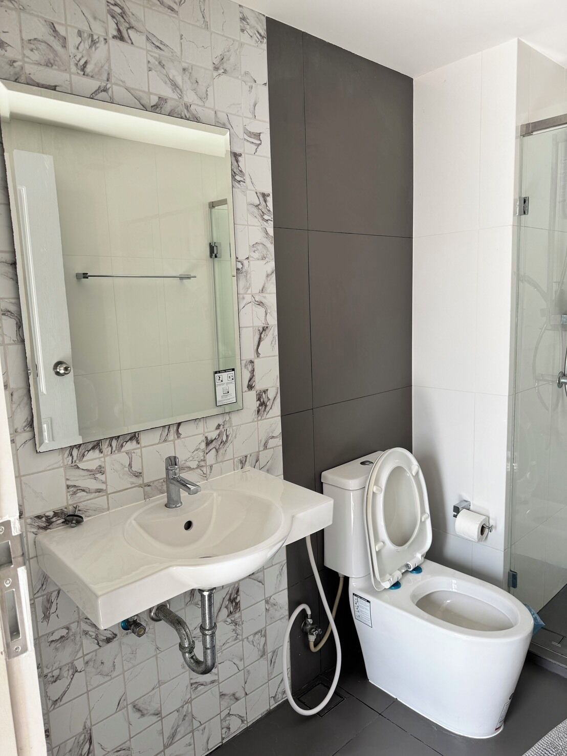 Een moderne badkamer met een betegelde muur van marmer, een wit wastafelmeubel, een toilet en een glazen douchecabine.