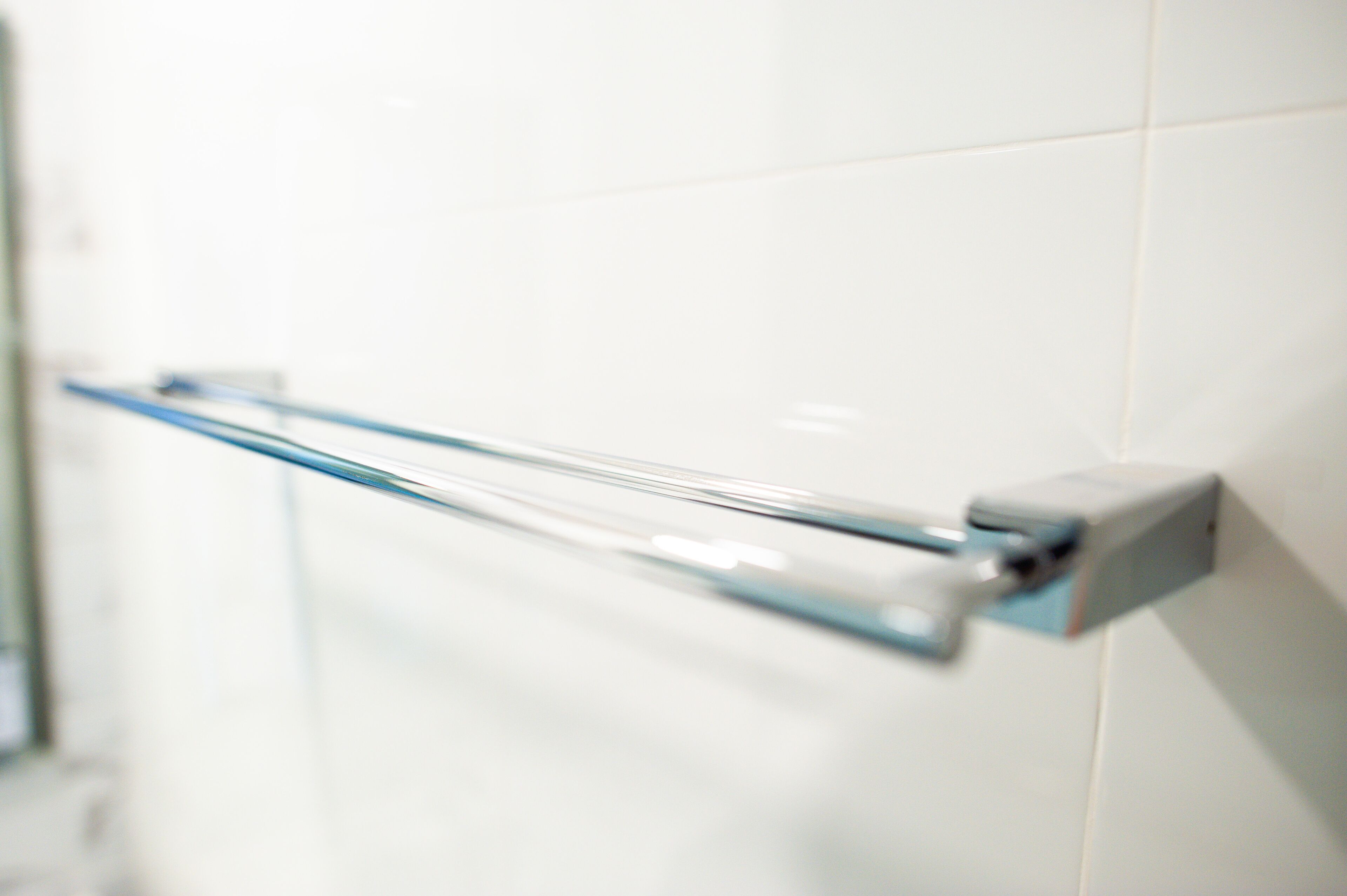 A bathroom with a glass towel rack mounted on a white tiled wall.