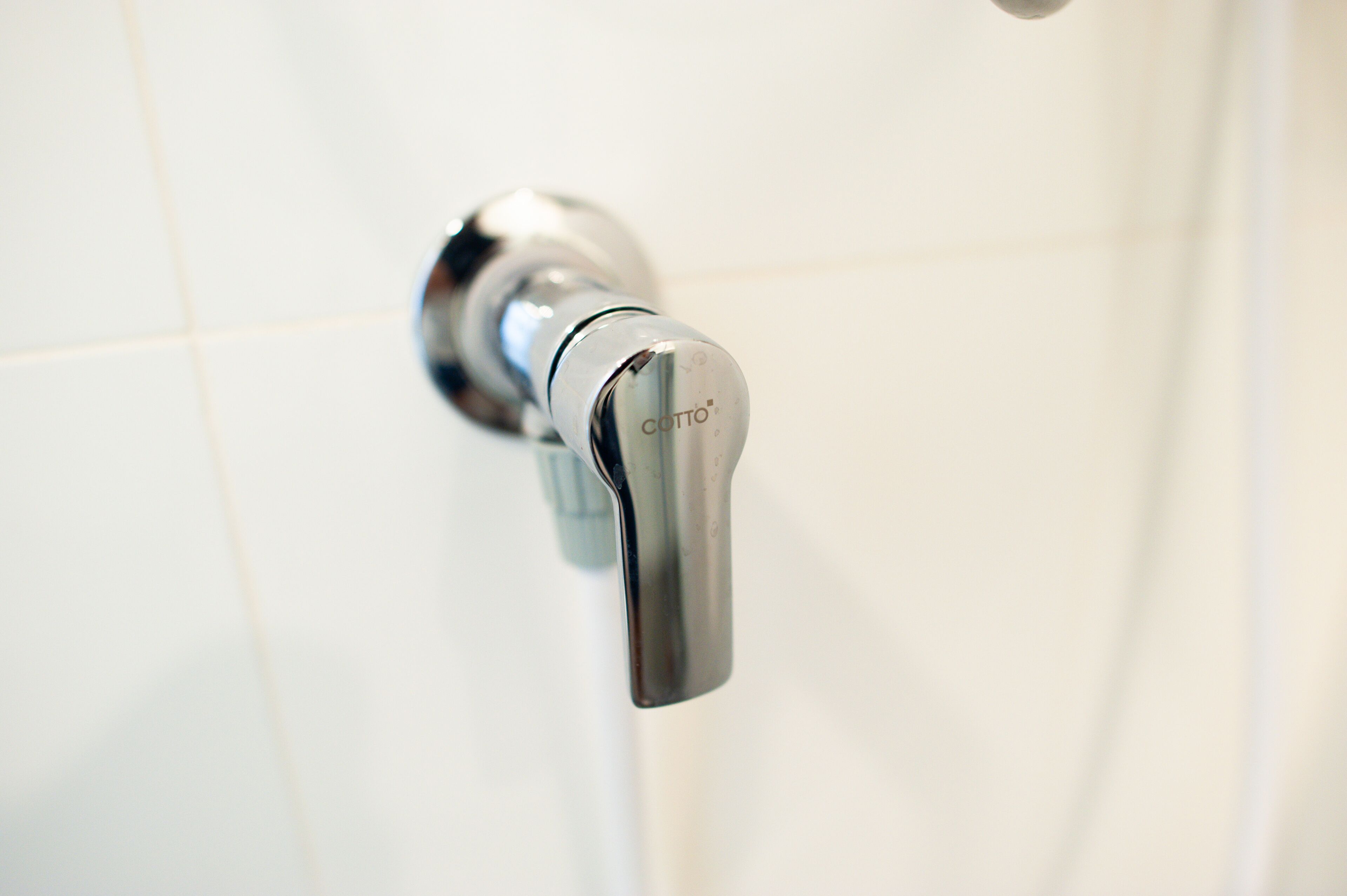 A chrome faucet with the brand name "COTTO" on a white tiled wall.