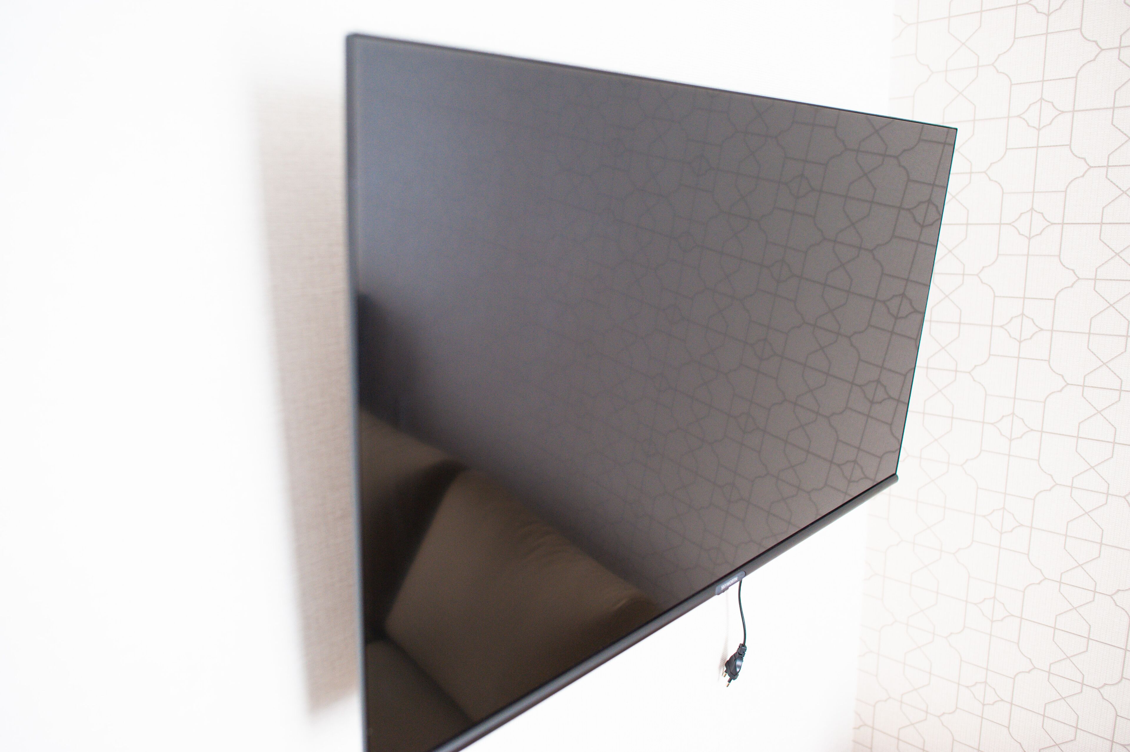 Un téléviseur à écran plat fixé au mur, avec un papier peint à motifs géométriques.