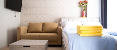 A modern hotel room with a sofa, a bed with yellow linens, a TV mounted on the wall, and a vase with flowers on the nightstand.