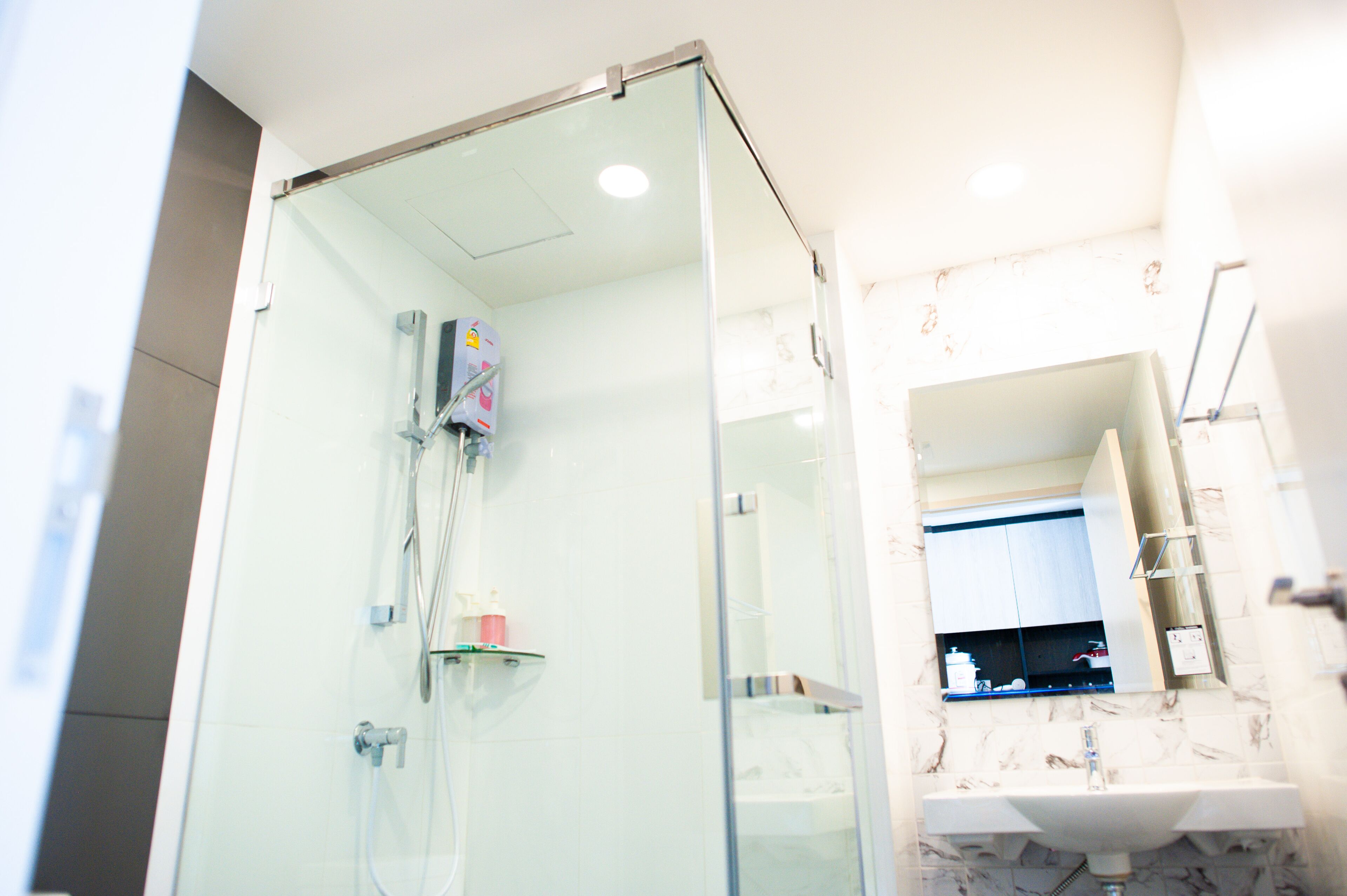 A modern bathroom with a glass-enclosed shower, a marble-tiled sink, and a built-in mirror.