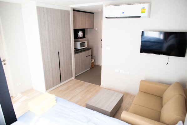 Quarto de hotel compacto com cama, sofá, TV de tela plana, micro-ondas e cozinha compacta.