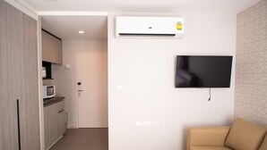 A modern living space with a kitchenette, a flat-screen TV mounted on the wall, and a beige sofa. - I'm Chinatown Residence (Bangkok)