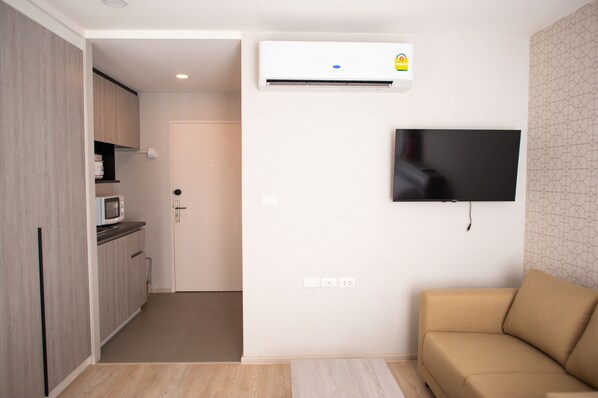 A modern living space with a kitchenette, a flat-screen TV mounted on the wall, and a beige sofa.