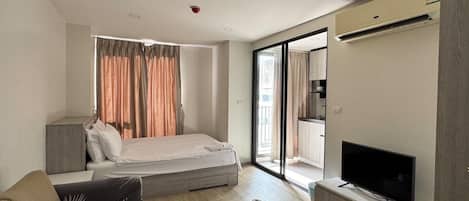 A modern hotel room with a bed, sofa, TV, and a sliding glass door to the balcony.
