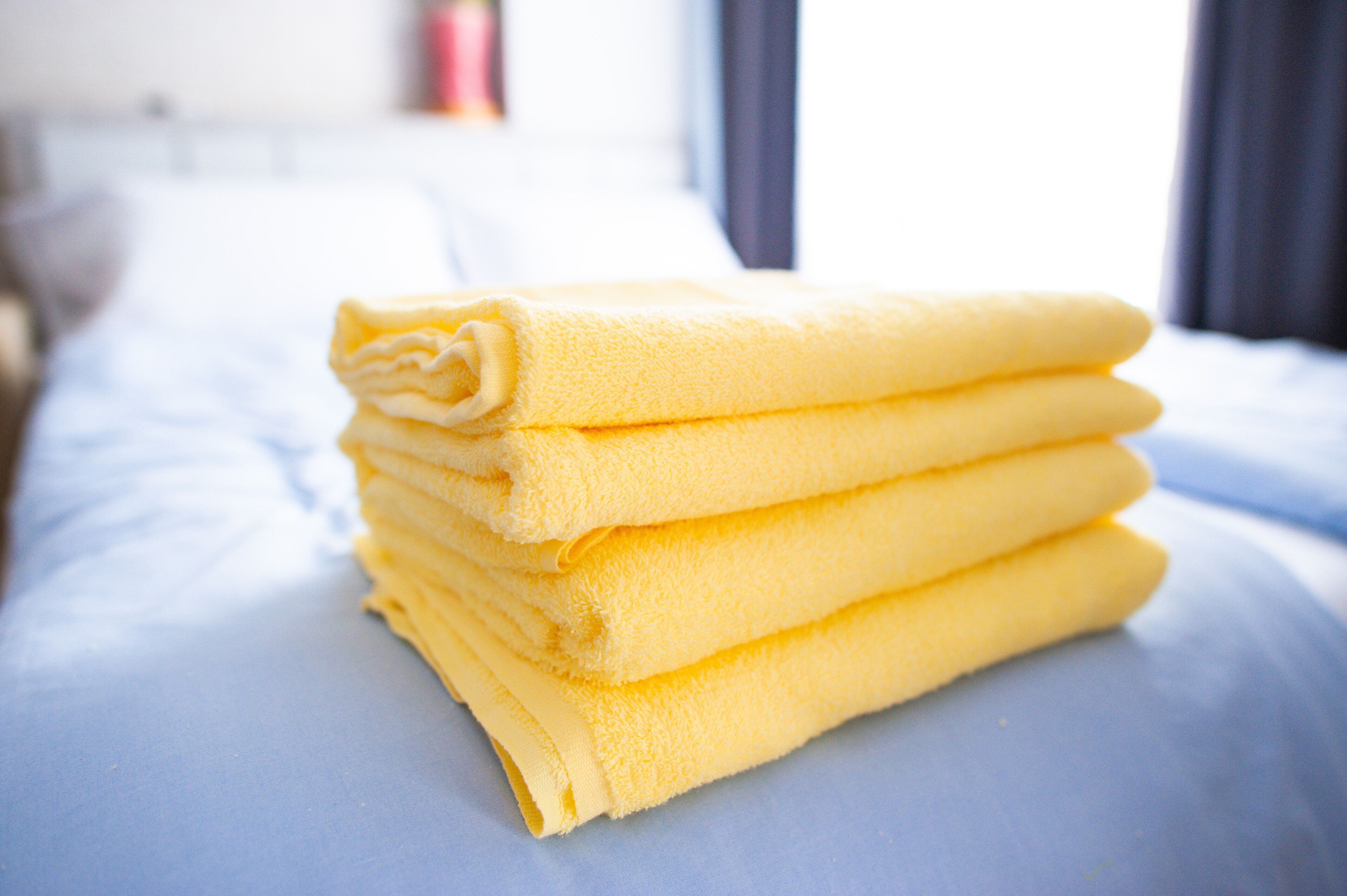 A stack of yellow towels on a bed with a blue bedspread.