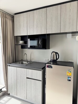 A compact kitchen with a built-in microwave, a Haier refrigerator, and a kettle on the counter. - I'm Chinatown Residence (Bangkok)