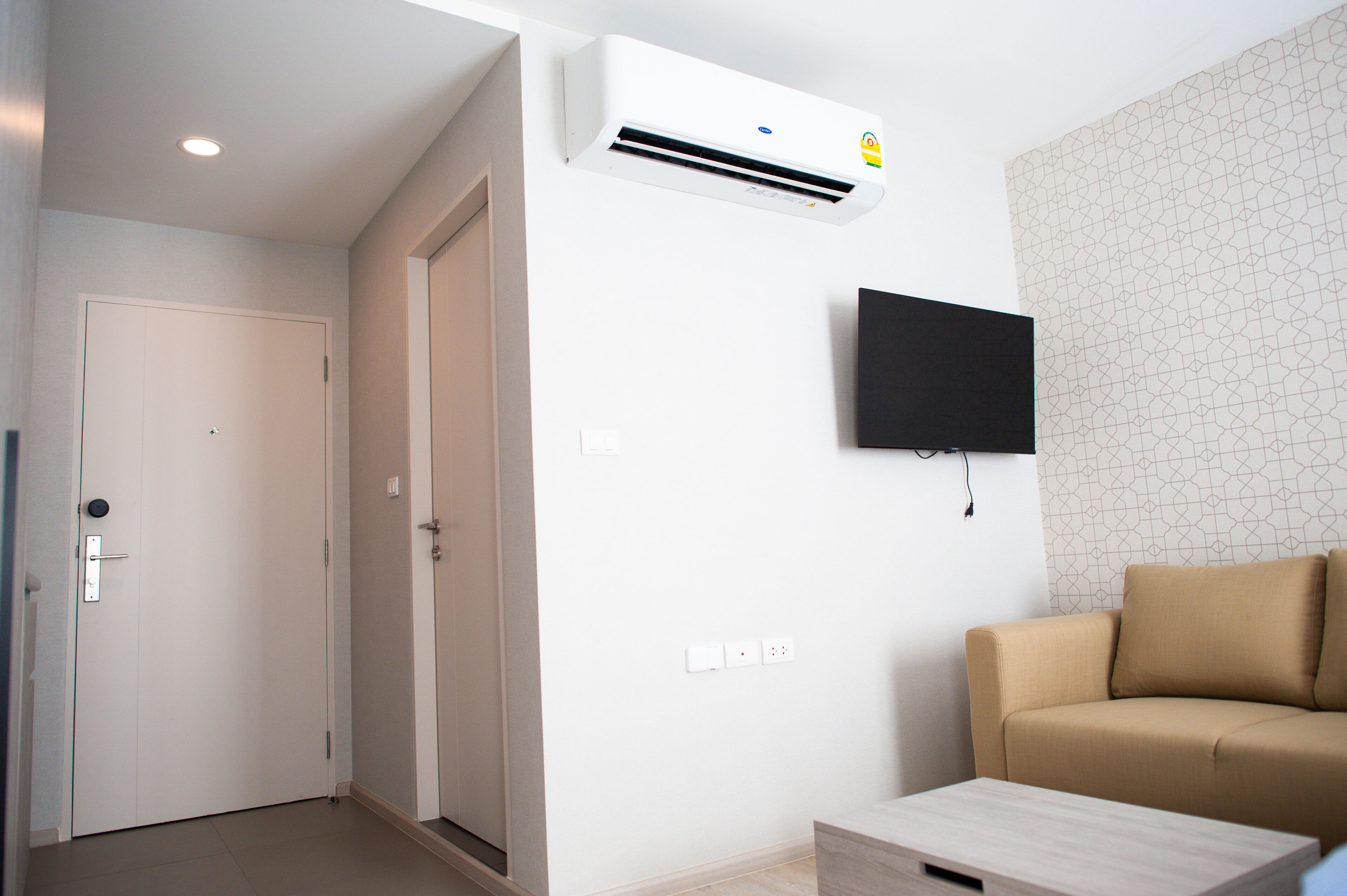 Ein modernes Wohnzimmer mit einem beigen Sofa, einem flachbildfernseher an der Wand und einer Klimaanlage über dem Sofa.