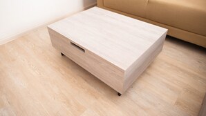 A light wooden bedside table with a drawer, positioned on a light wooden floor next to a beige sofa. - I'm Chinatown Residence (Bangkok)
