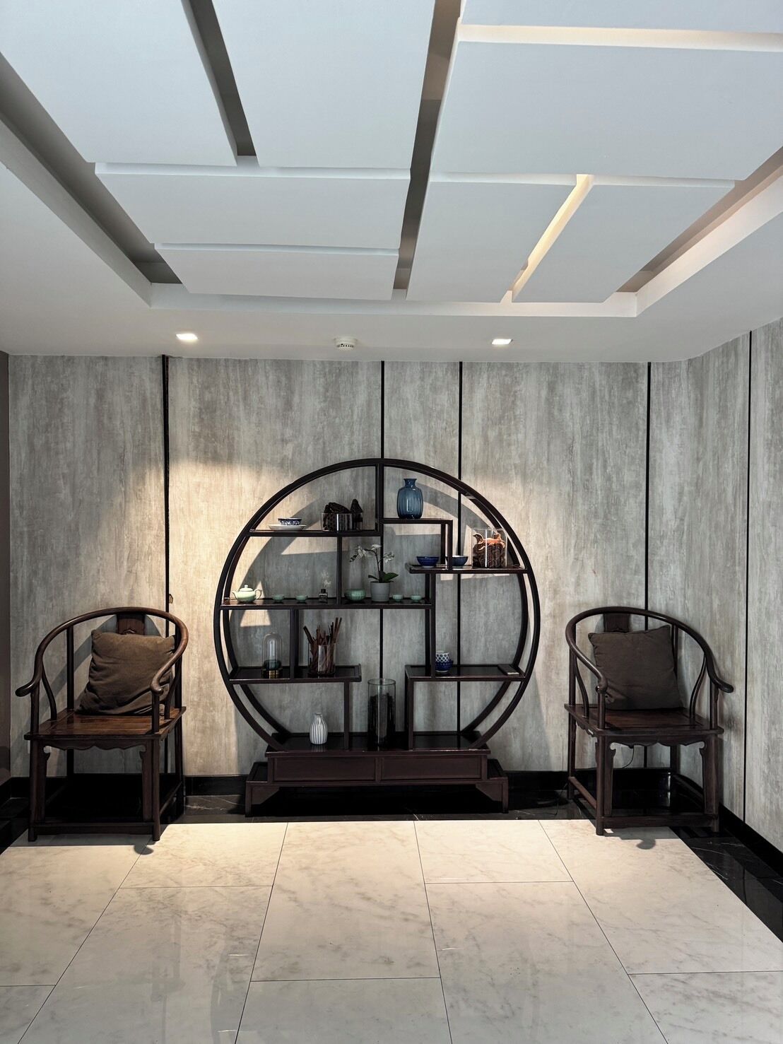 A modern interior with two wooden chairs, a circular shelving unit, and a recessed ceiling.