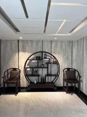 A modern interior with two wooden chairs, a circular shelving unit, and a recessed ceiling. - I'm Chinatown Residence (Bangkok)