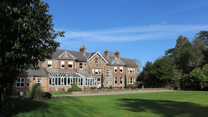 A large, multi-story building with a conservatory, surrounded by a well-maintained lawn and trees. - Burn Hall Hotel (York)