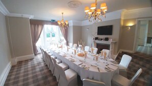 A formal dining room with a long table set for a meal, a chandelier, and a fireplace. - Burn Hall Hotel (York)