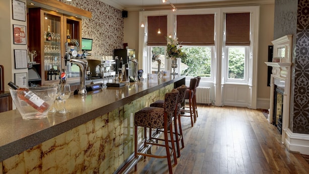 A bar area with a marble countertop, bar stools, and a view of the outdoors through large windows. - Burn Hall Hotel (York)
