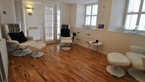 A room with wooden flooring, a white radiator, two chairs with footrests, a small table, and a window with blinds. - Oyster Cottage- relaxing retreat by the sea (Saint Monans)