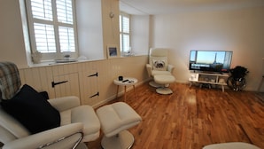 A modern living room with a sofa, armchair, and ottoman, a television, and a small table with a plant. - Oyster Cottage- relaxing retreat by the sea (Saint Monans)