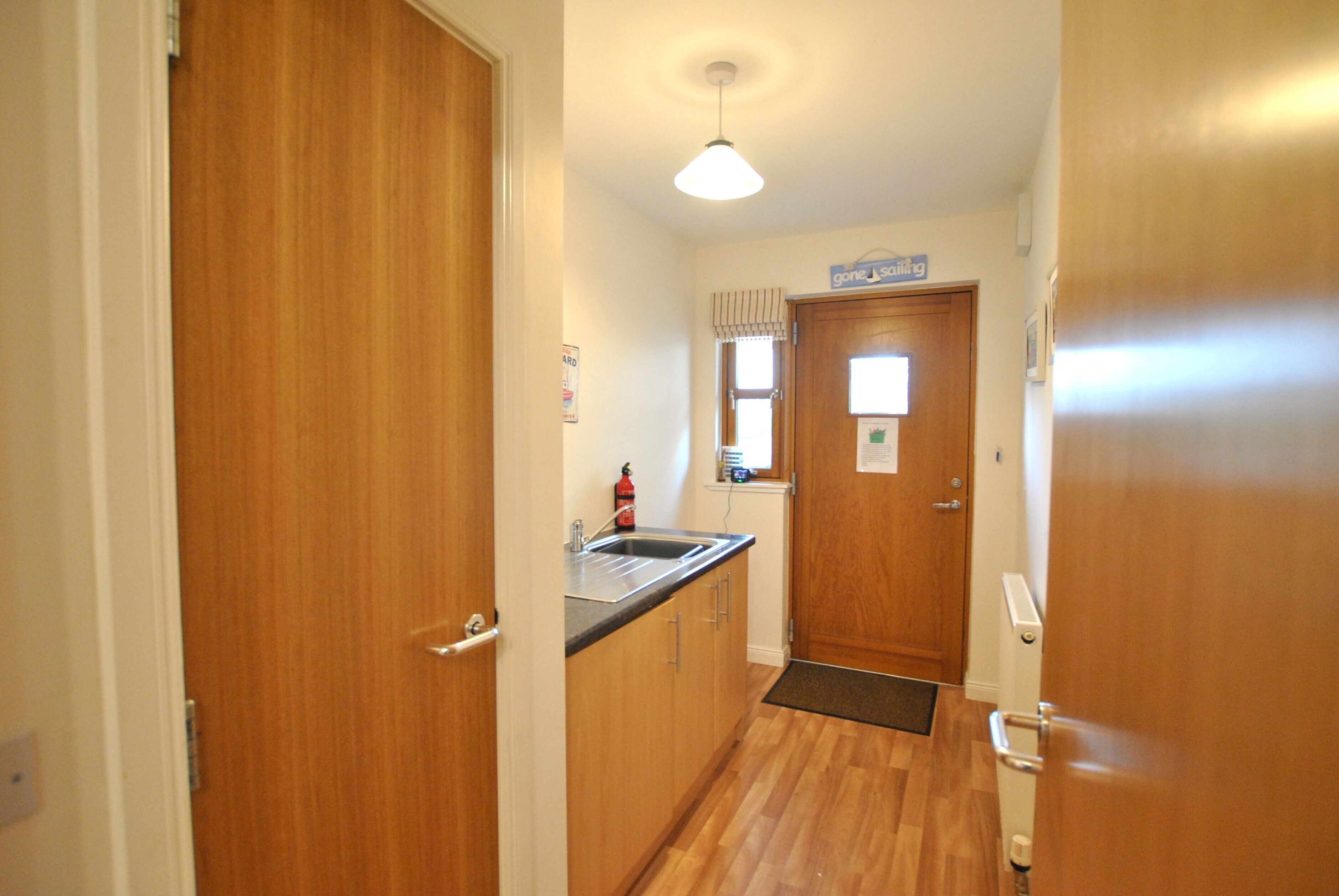 A narrow kitchen with wooden cabinets, a stainless steel sink, and a window with blinds.