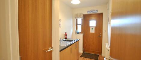 A narrow kitchen with wooden cabinets, a stainless steel sink, and a window with blinds.