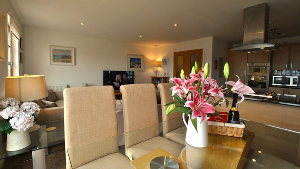 A modern living room with a glass coffee table, beige sofas, and a vase of pink flowers.