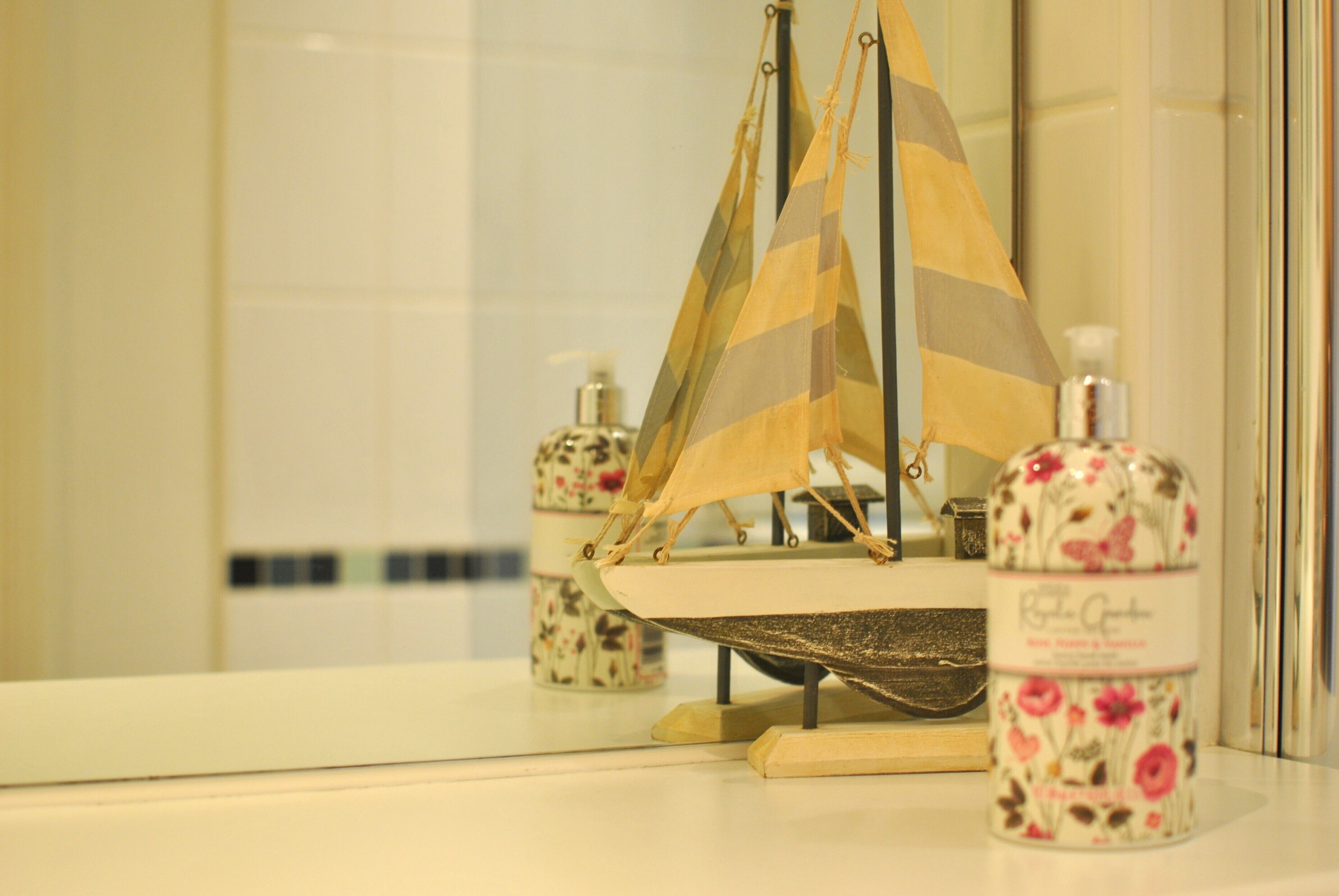 Un baño con un pequeño modelo de velero, un dispensador de jabón floral y un espejo.