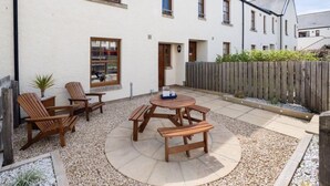 A white building with a patio area featuring wooden furniture and a round table.