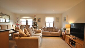 A living room with a beige sofa, a television, and a Christmas tree.