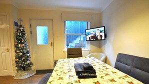 A room with a Christmas tree, a television mounted on the wall, and a table with a floral tablecloth.