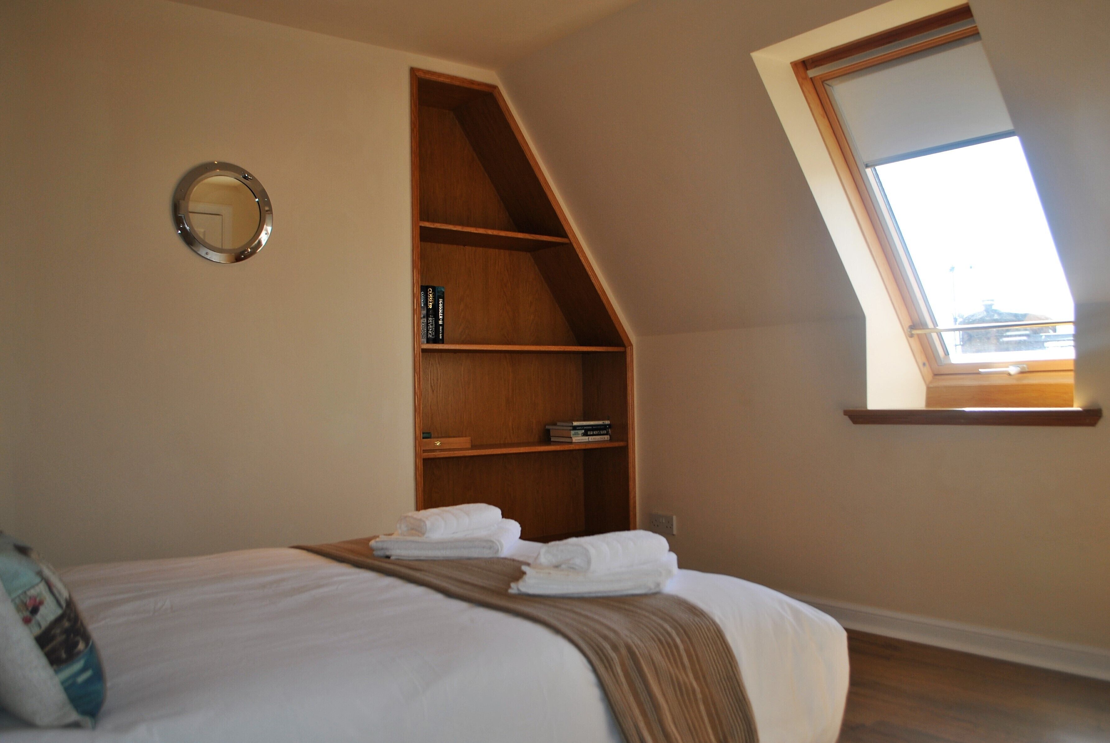 A bedroom with a bed, a wooden shelf, a mirror, and a skylight.