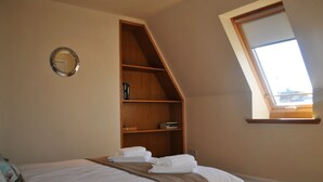 A bedroom with a bed, a wooden shelf, a mirror, and a skylight.