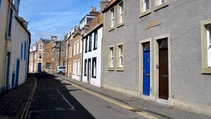 A narrow street lined with historic buildings, featuring a mix of architectural styles and a clear road with double yellow lines.