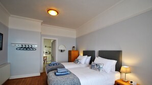A bedroom with a large bed, bedside tables, a nightstand with a lamp, a coat rack, and a mirror. - Gyles Apartment - harbourfront studio, Pittenweem (Pittenweem)