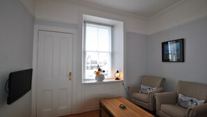 A living room with a wooden coffee table, two armchairs, a white door, and a window with blinds. - Gyles Apartment - harbourfront studio, Pittenweem (Pittenweem)