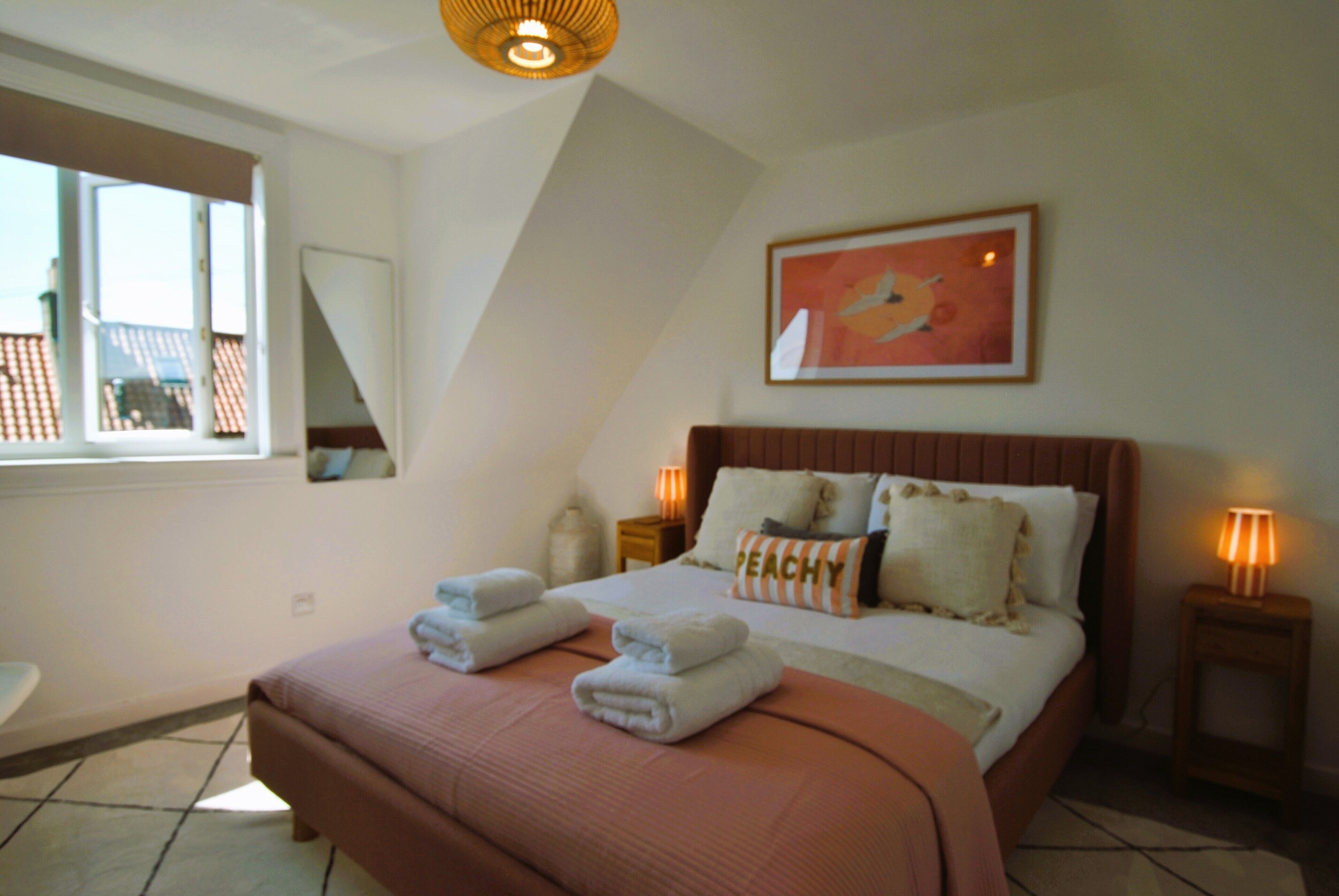 A bedroom with a large bed, a window, and a painting on the wall.