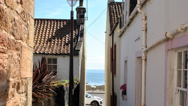 Une ruelle étroite, un chien, un lampadaire et une vue sur la mer.