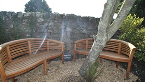 Two wooden benches with slatted backs and seats, placed on a gravel surface with a stone wall in the background. A sign reading "Mariners' Retreat" is visible between the benches. - Mariners Retreat- spacious apartment in Crail (Crail)