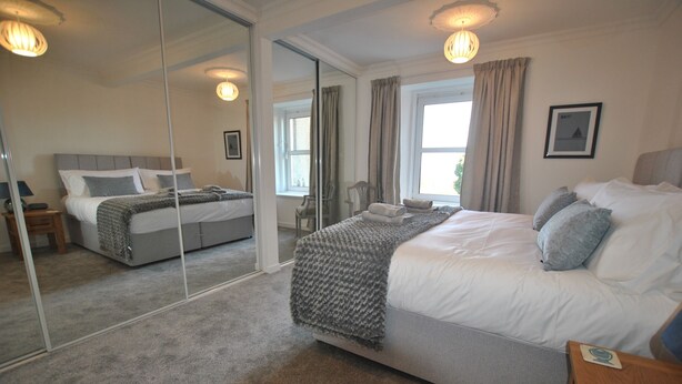 A bedroom with a large bed, a mirror, a window with curtains, and a bedside table. - Mariners Retreat- spacious apartment in Crail (Crail)
